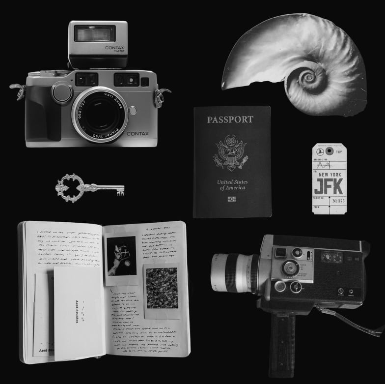 A rangefinder camera, passport, nautilus shell, key, luggage tag, open journal and Super-8 camera arranged on black